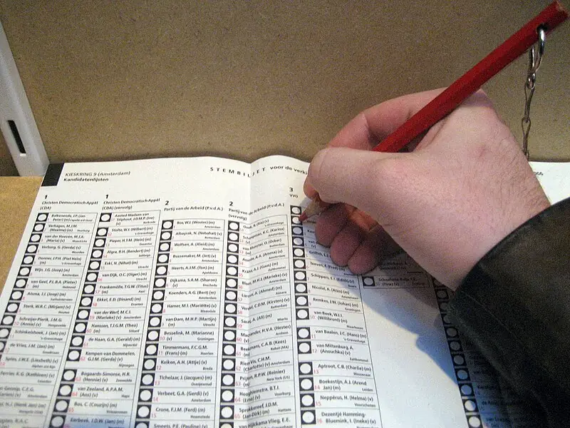 A person ticking a box on a ballot sheet with a red chained up pen.