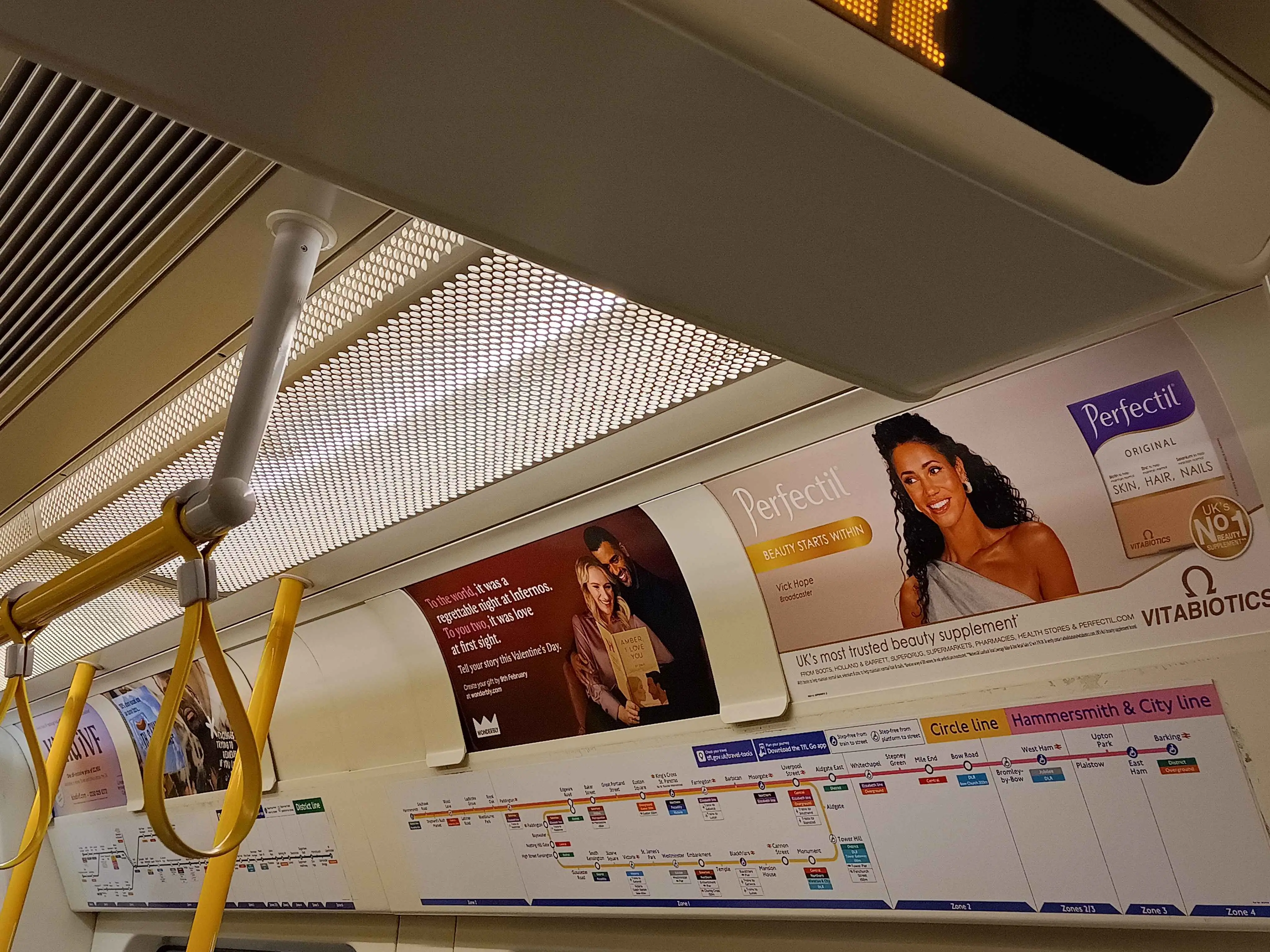 An S7 stock train, showing the line maps accompanied with adverts, with the District Line map on the left and the combined C and H map on the right.